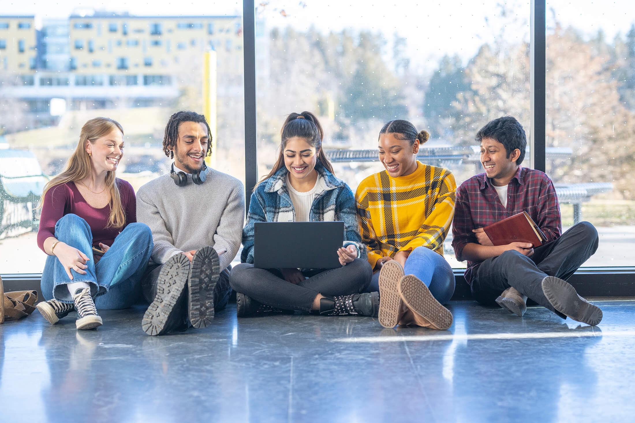 A small group of diverse University students sit on the floor, side-by-side as they work together.