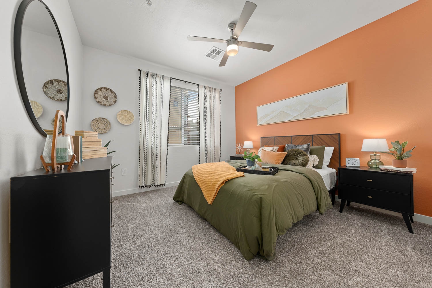 A modern bedroom with an orange accent wall and a large bed with green and orange bedding.